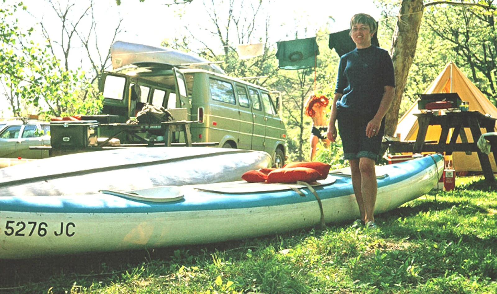 A person stands beside a canoe at a wooded campsite.